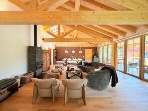 A spacious living area with a high ceiling and large windows, wooden beams, and a fireplace. - La Tzoumaz Lodge – Luxury Chalet with Daily Housekeeping, Optional Private Chef (Riddes)