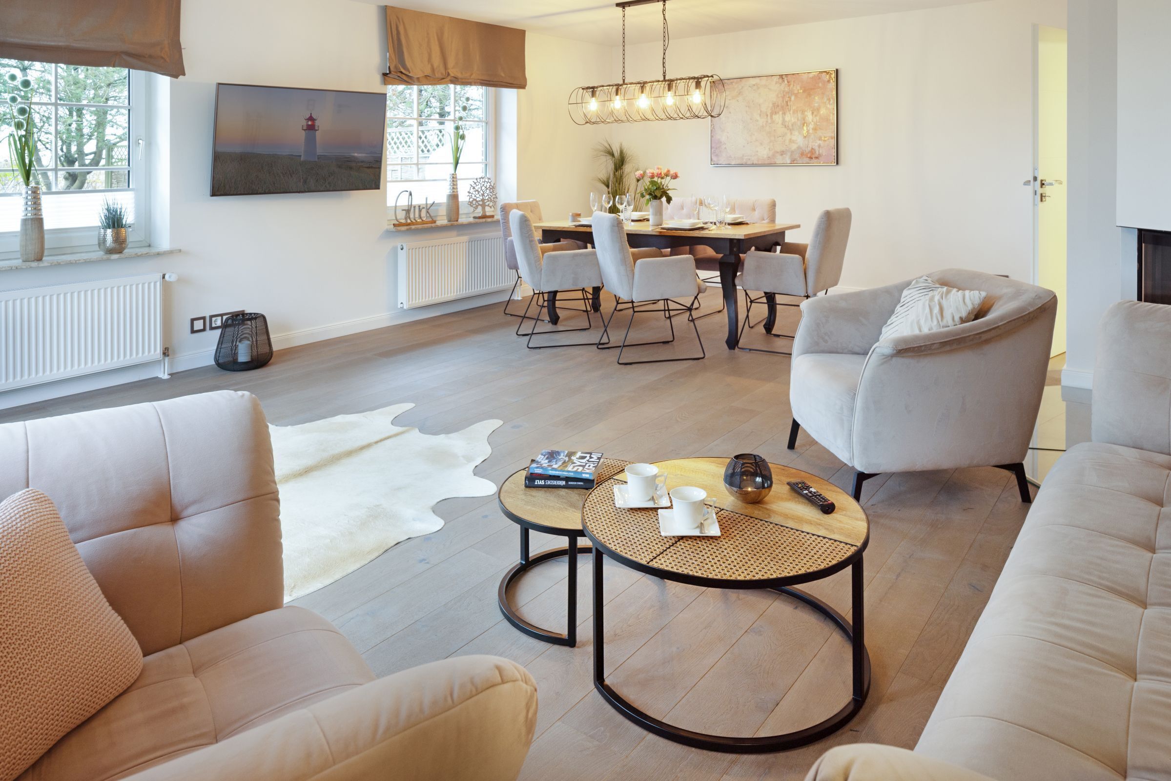Ein modernes Wohnzimmer mit einer Couch, Sesseln, einem Couchtisch und einem Essbereich mit Tisch und Stühlen.