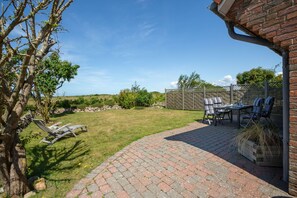 Een terras met een metselstenen vloer, tuinmeubilair en uitzicht op het omliggende landschap.