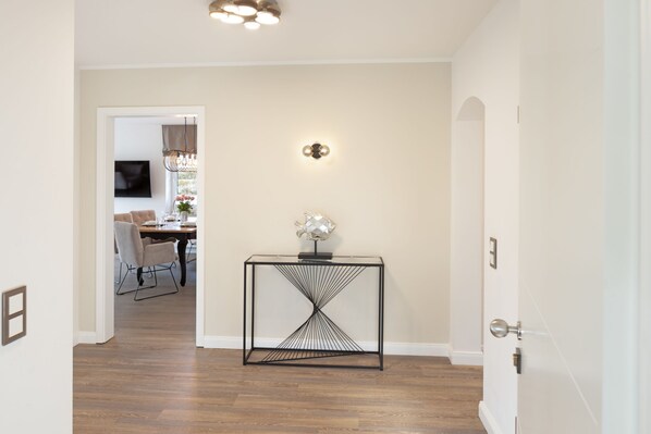 A hallway with a modern console table, a wall-mounted light fixture, and a door leading to another room.