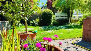 Un jardin où l’on trouve une grande variété de plantes et de fleurs, un mur en briques et, au fond, une clôture en bois.