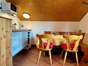 Una cocina compacta con armarios de madera, microondas y un comedor con dos sillas de madera y una mesa.