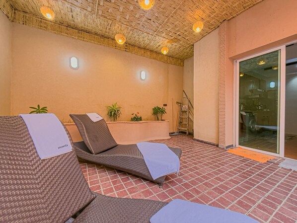 A sunlit lounge area with wicker chairs, a small table, and potted plants.
