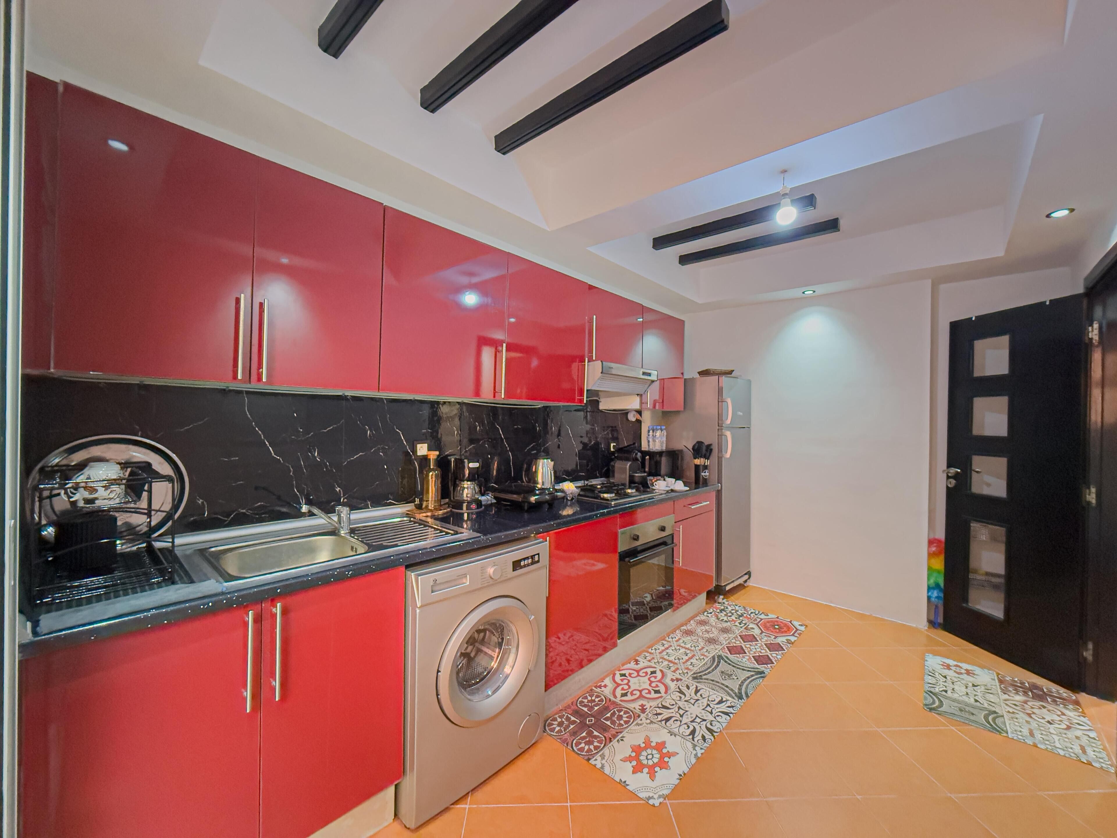 Una cucina moderna con mobili rossi, una lavatrice e un pavimento piastrellato.