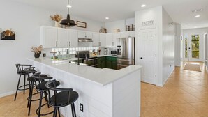 Una cocina moderna con armarios blancos, una isla grande con taburetes de bar, electrodomésticos de acero inoxidable y una puerta de despensa.