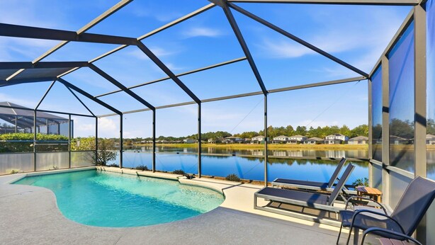 Una piscina techada al aire libre con sillas reclinables y vistas a un lago y casas al fondo.