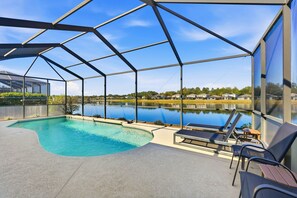 Una piscina techada al aire libre con sillas reclinables y vistas a un lago y casas al fondo.
