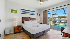 Un dormitorio con cama, mesitas de noche, ventilador de techo y vistas a una piscina.
