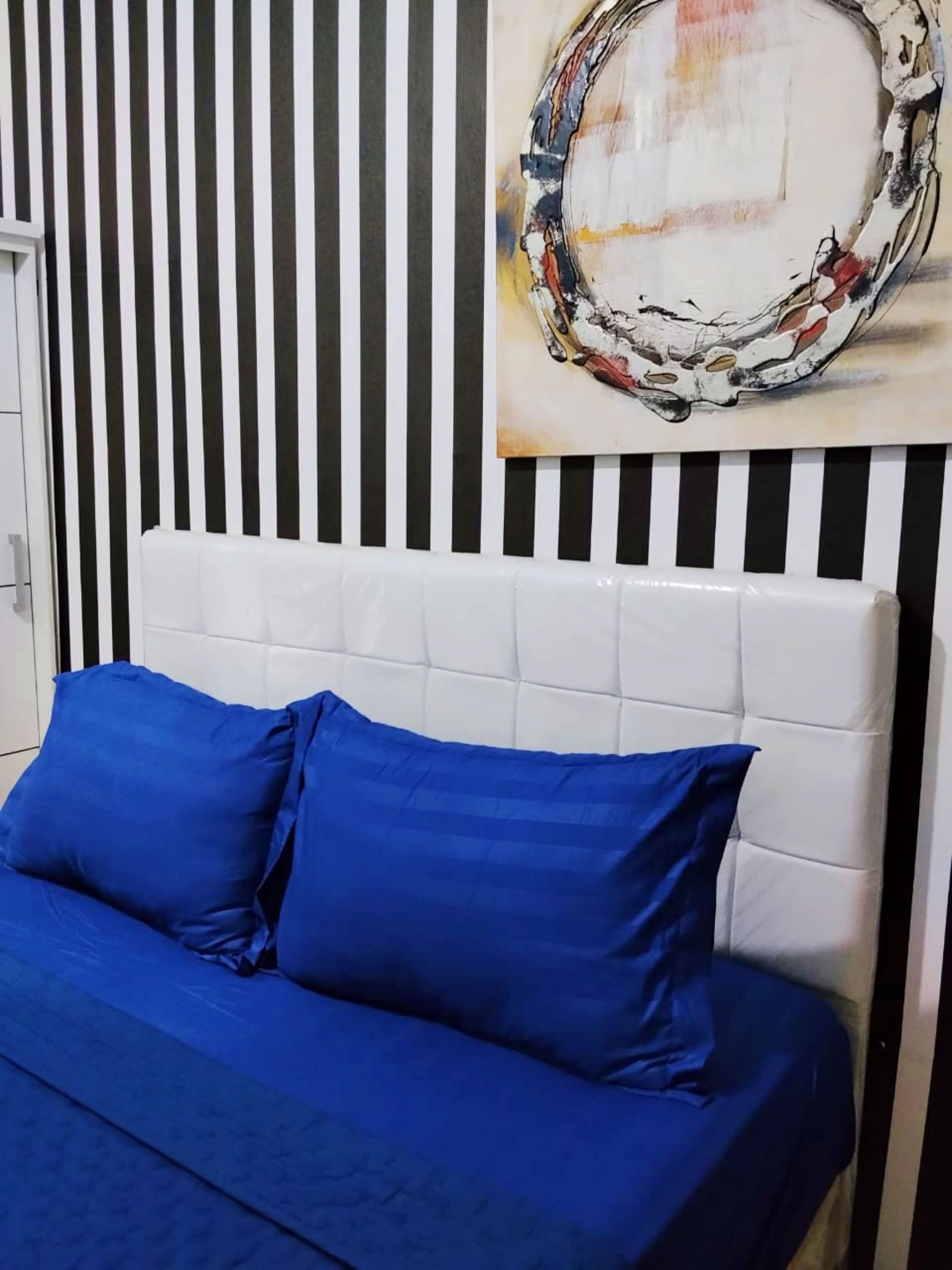 A bed with blue bedding and a white headboard against a striped wall.