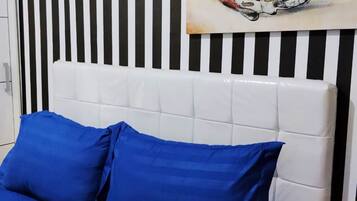 Llits amb roba de llit blava i un panell de capçal blanc davant d'una paret amb ratlles.