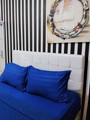 Un lit avec une literie bleue et une tête de lit blanche, le tout placé devant un mur à rayures.