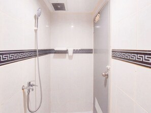 Un petit espace douche fermé, équipé d’un pommeau de douche à main et d’un robinet fixé au mur.