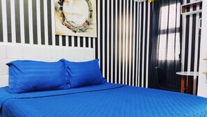 Una cama con ropa de cama azul, un cabecero blanco y una pared a rayas con una obra de arte circular en la parte superior.