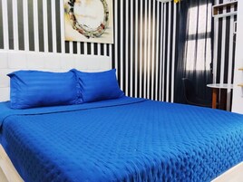 A bed with blue bedding, a white headboard, and a striped wall with a circular artwork above it.