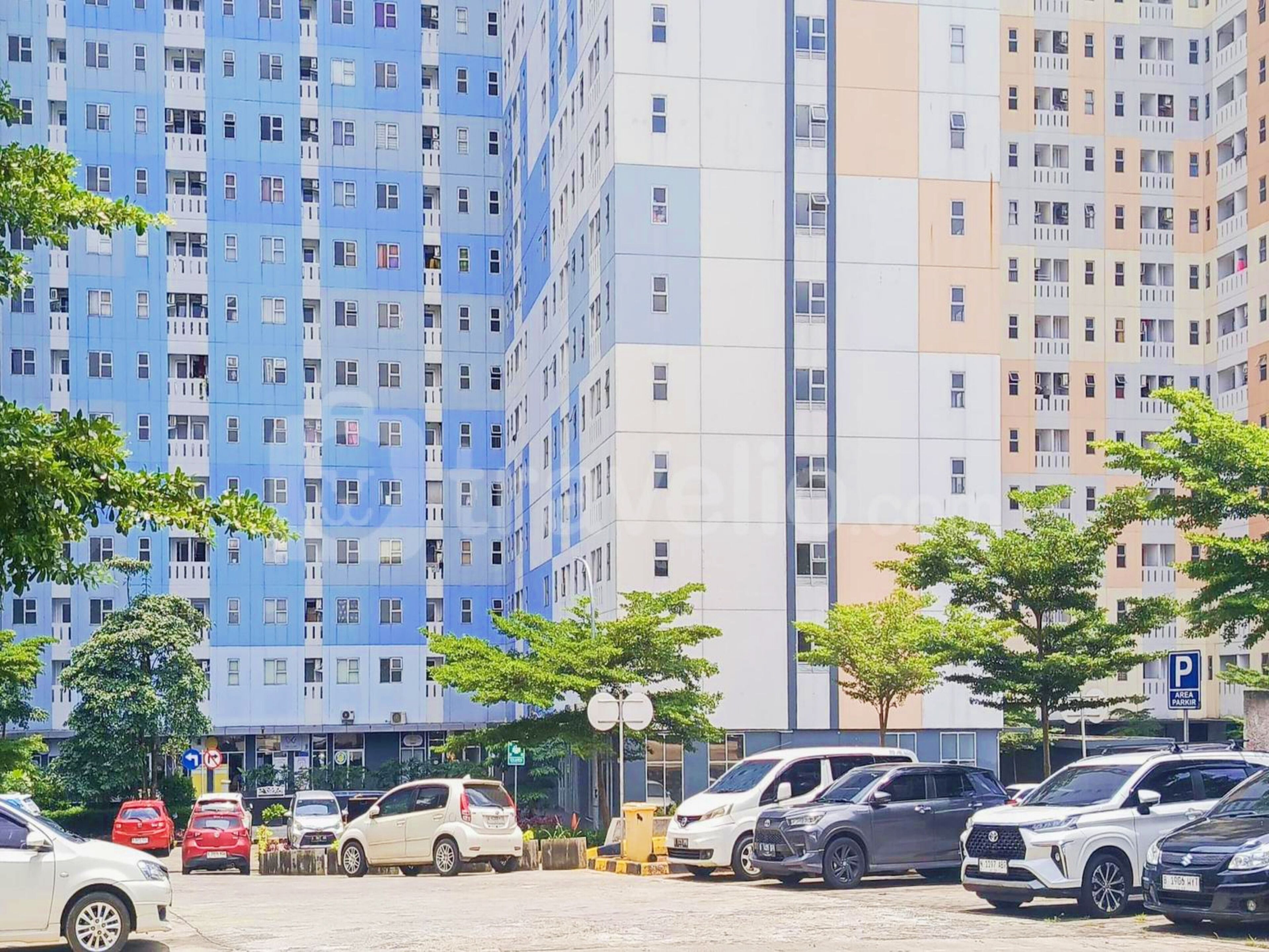 Un parking avec plusieurs voitures, un immeuble à étages aux façades bleues et beiges, et un panneau indiquant une zone de stationnement.