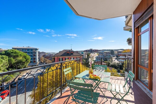 Varanda com mesa posta para refeições, vista para paisagem urbana com diversos edifícios e árvores.