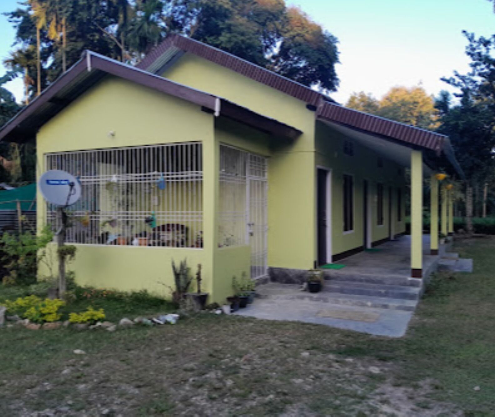 Un edificio de una sola planta con fachada amarilla, un porche cubierto y una antena parabólica.