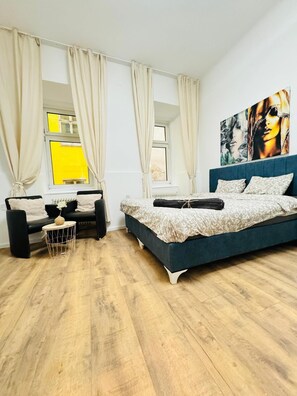 A modern bedroom with a large bed, a sofa, a small side table, and a window with curtains. - 5BR Apartment Near Matzleinsdorfer (Vienna)