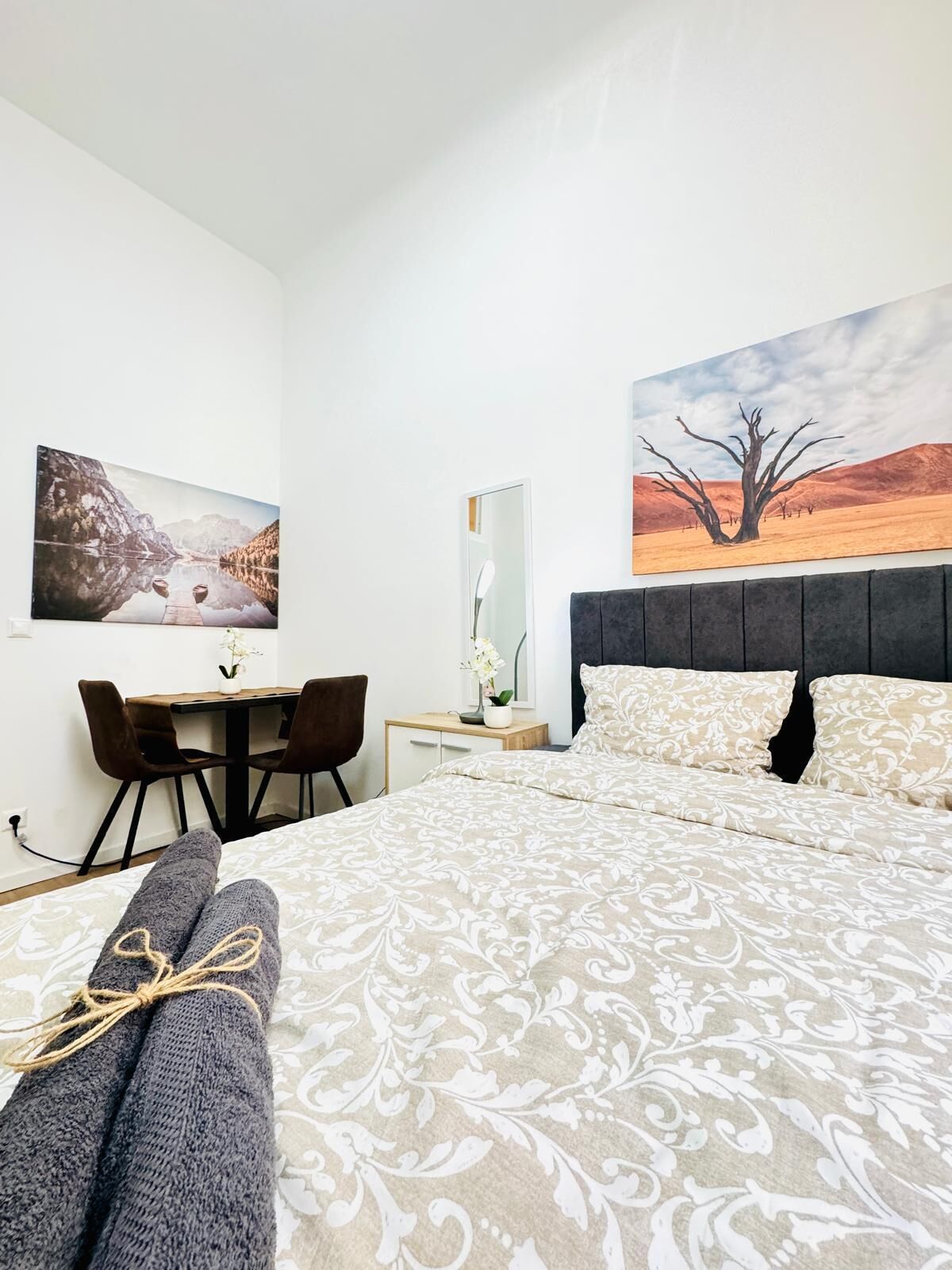 Ein Hotelzimmer mit einem Bett, einem Schreibtisch und zwei Stühlen. An den Wänden hängen zwei Gemälde.
