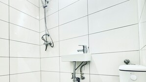 Ein Badezimmer mit weiß gefliesten Wänden, einer weißen Toilette, einem Duschkopf und einem Boden mit Marmoroptik.