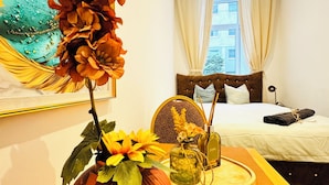 Ein Hotelzimmer mit einem Bett, einem großen Gemälde, einer Vase mit Blumen und einem Holztisch mit einer Flasche und einer Kerze.