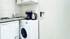 Eine kleine Küche mit Waschmaschine, Kaffeemaschine und Durchlauferhitzer.