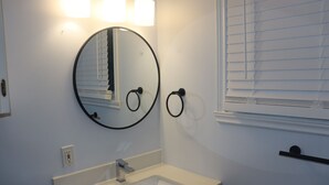 A bathroom with a round mirror, a sink, and a towel ring. - Guest Favourite 3BR Home | Walk Downtown | Parking (Fredericton)