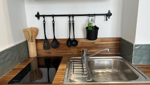 Een moderne keuken met een roestvrijstalen spoelbak, een houten aanrechtblad en een zwarte houder voor keukengerei met spatels en een opscheplepel.