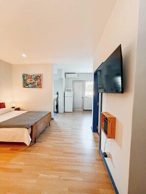 Una camera da letto con un letto, una TV a muro e un angolo cottura sullo sfondo.