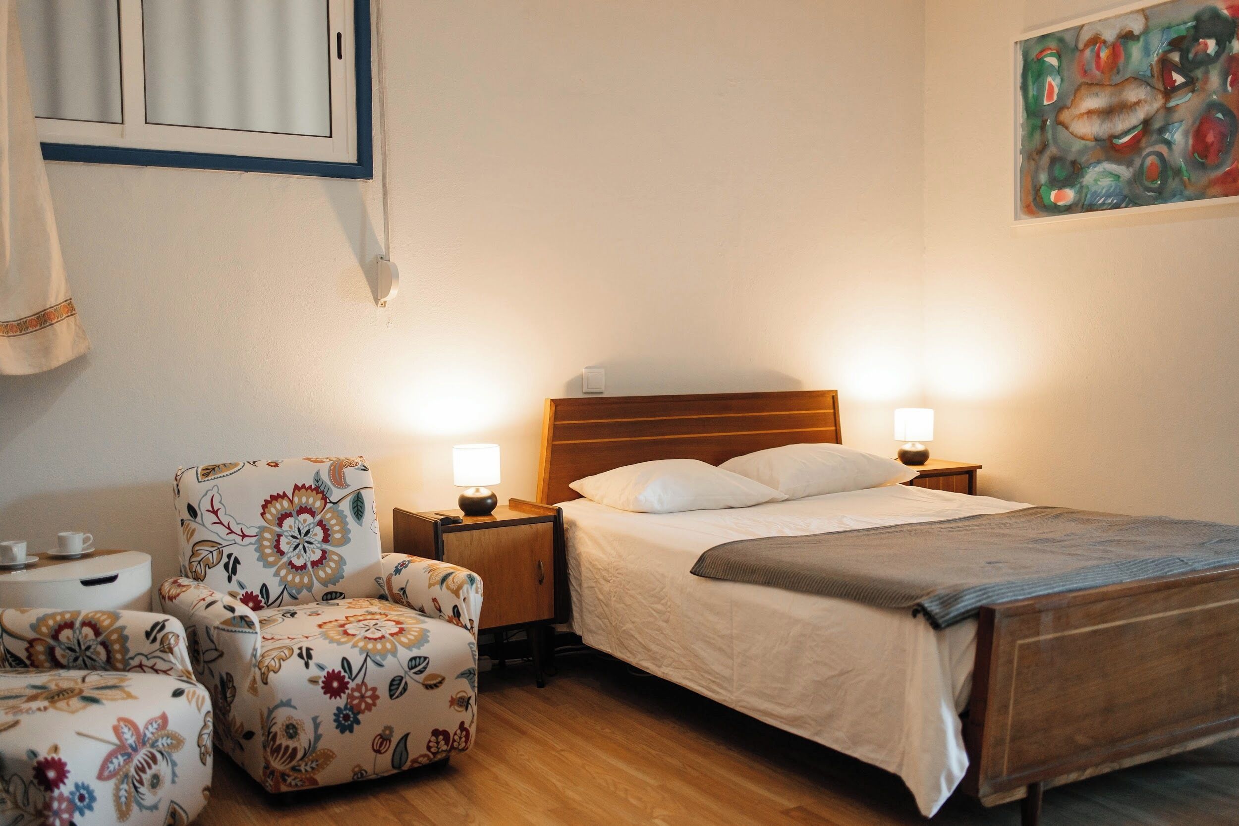 A bedroom with a bed, two bedside tables with lamps, a floral armchair, and a wall-mounted cabinet.
