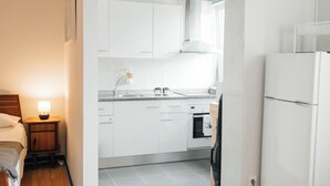 A modern kitchen with white cabinets, a built-in oven, and a refrigerator. - Cozy studio in Porto (Porto)