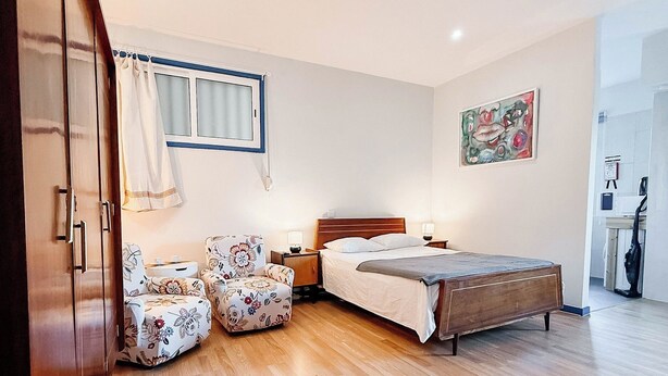 A bedroom with a wooden floor, a bed, a chair, a nightstand, and a window with curtains. - Cozy studio in Porto (Porto)