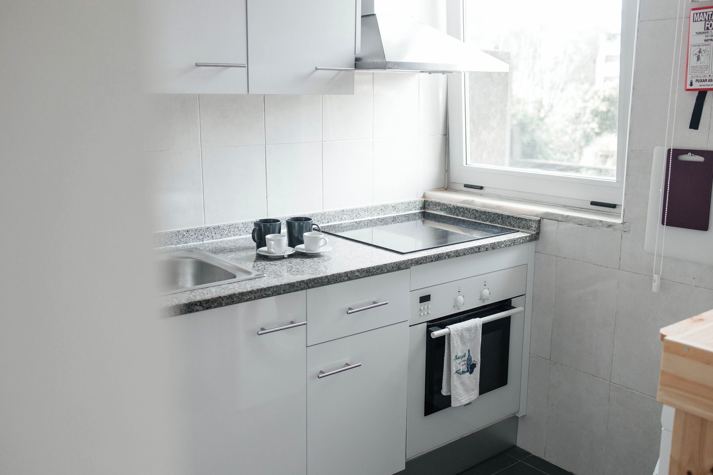 Een keuken met witte kasten, een granieten aanrechtblad, een roestvrijstalen spoelbak en een inbouwoven.
