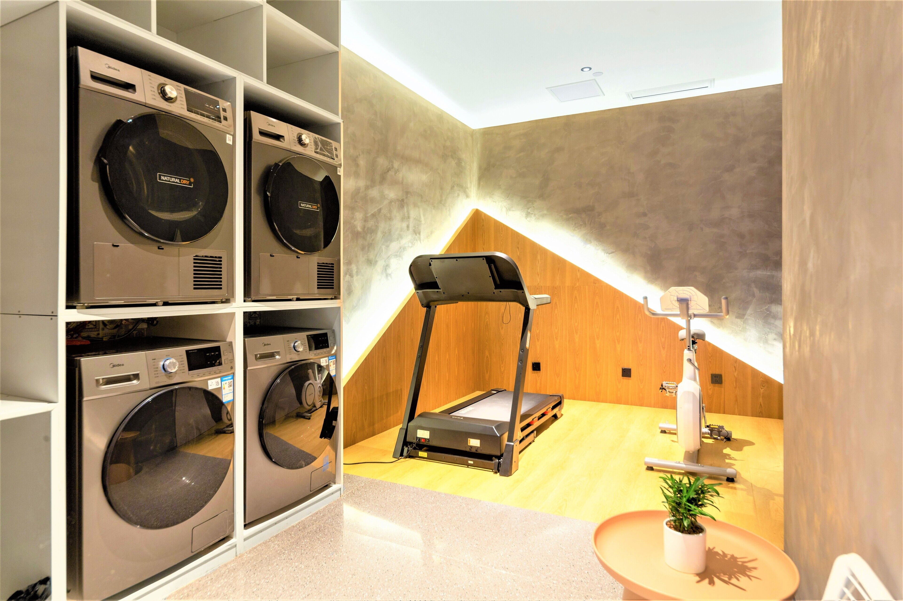 A laundry room with stacked washing machines and a treadmill.