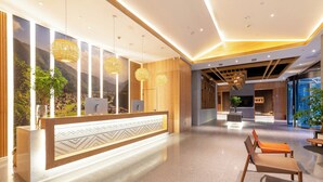 A modern reception area with a reception desk, seating area, and a view of mountains through large windows. - TRUE Go hotel (Chengdu)