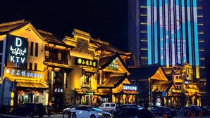 A traditional building with illuminated signage, a modern high-rise building in the background, and parked cars on the street. - TRUE Go hotel (Chengdu)