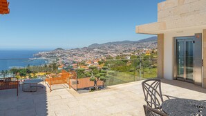 Un balcon avec une table et des chaises, une vue sur une ville côtière et un bâtiment doté d’une porte en verre.