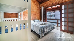 Ein Schlafzimmer mit einem Bett, einer weißen Trennwand mit Fenstern, einer Backsteinwand und einer großen Schiebeglastür.