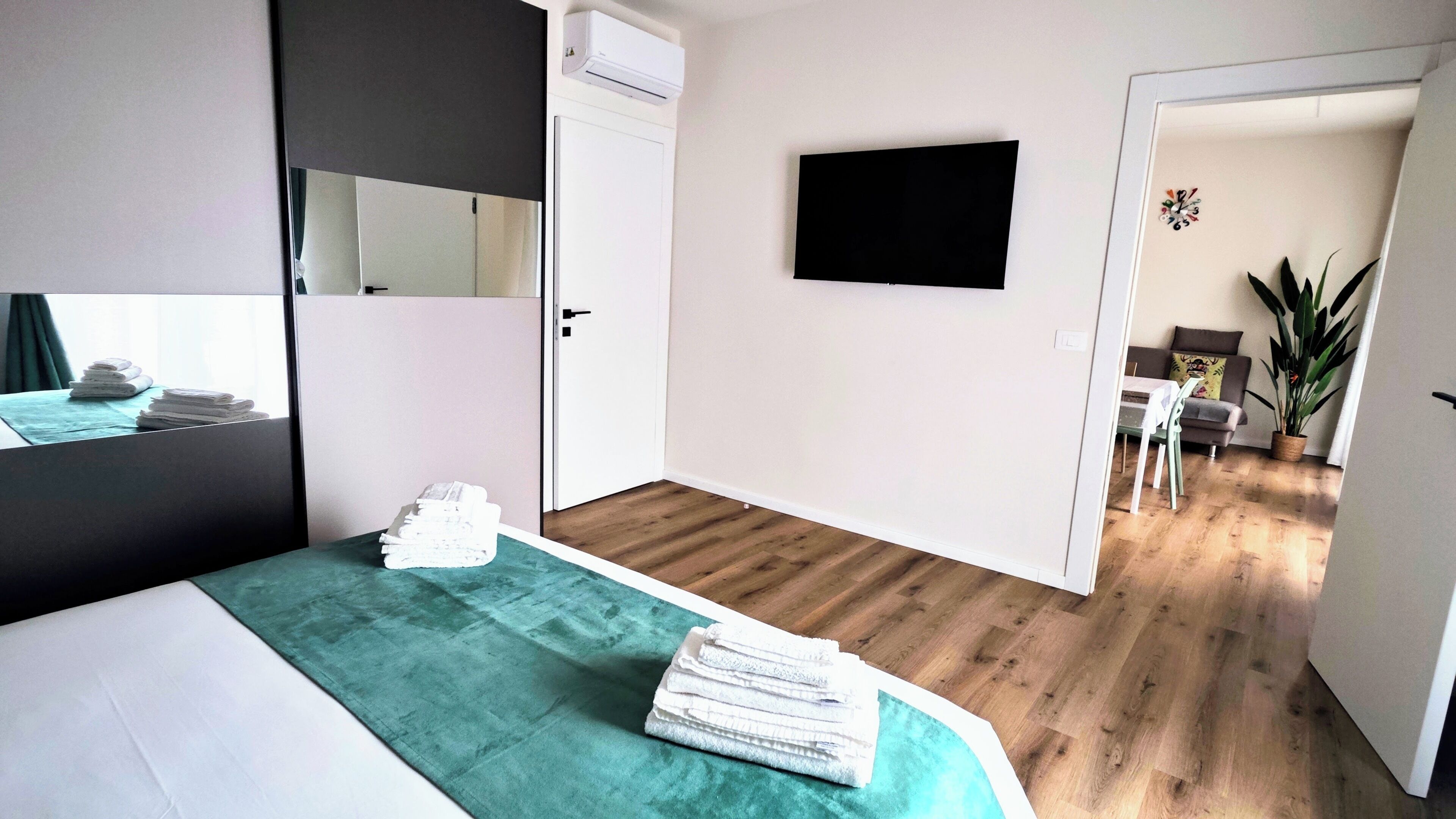 A hotel room with a bed, a mirror, a TV, and a view into the living area.