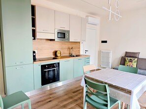 A modern kitchen with a microwave, oven, and sink. There is a dining table with chairs and a radiator. - Sweet SN Suite - Junior Suite con Idromassaggio & Apartment - Vacation Rental - Monopoli (Monopoli)