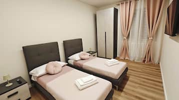 Una camera d'albergo con due letti, un comodino con una lampada, un armadio e una TV a muro.