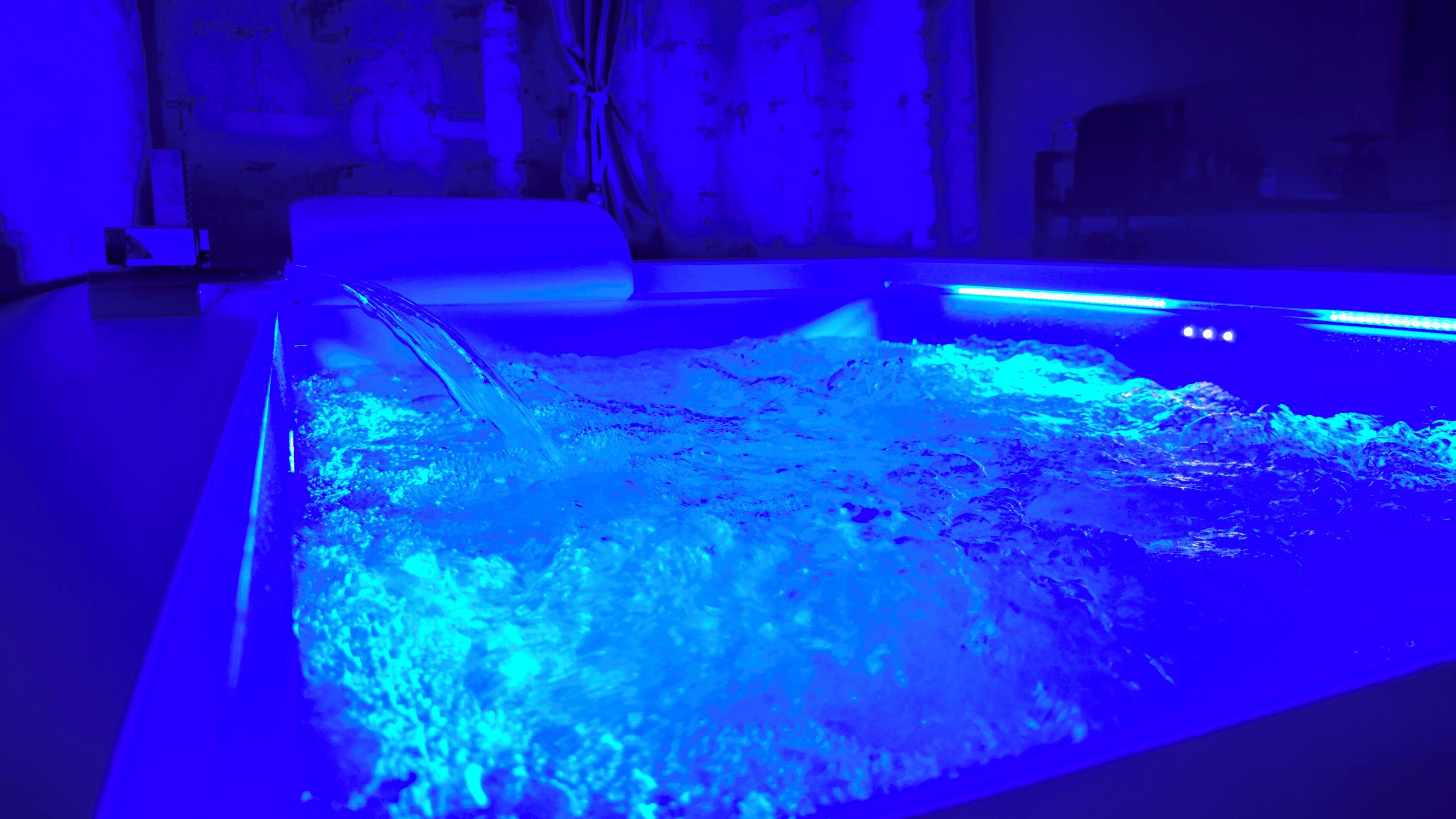 A room with a large, rectangular water feature in the center, a bed with a headboard, and a wall with a patterned design.
