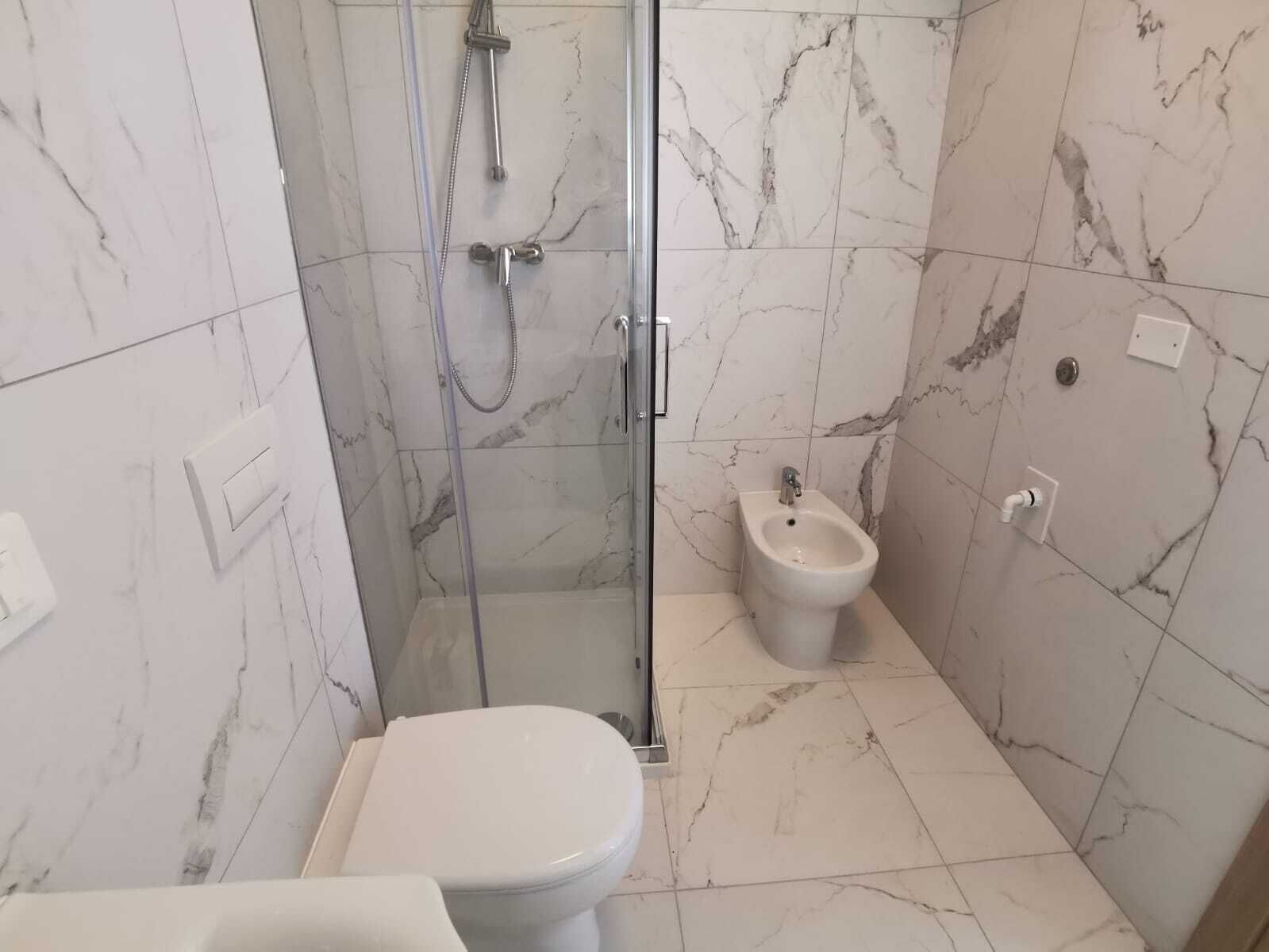 Kylpyhuone, jossa on wc, bidee ja lasiseinällä varustettu suihku.