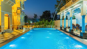 A swimming pool with a tiled deck, surrounded by traditional architecture with columns and arches. - Aryavarta A boutique abode (Udaipur)