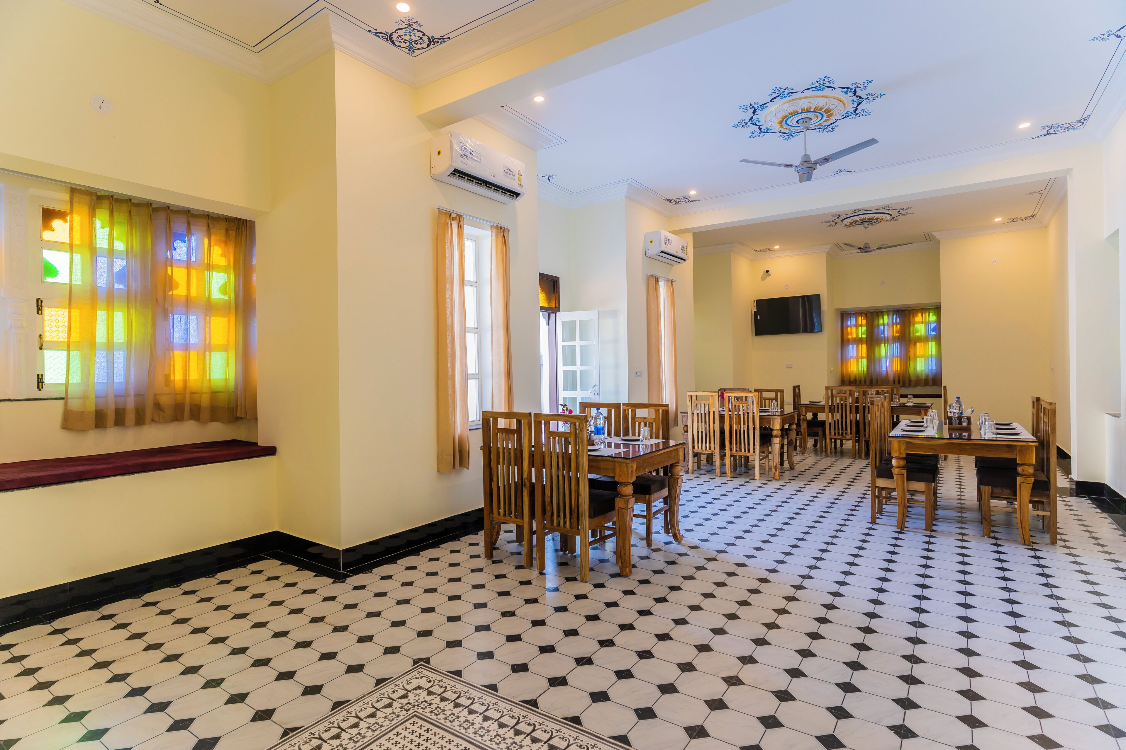 Un comedor de hotel con suelo de patrón hexagonal, mesas y sillas de madera, y ventanas con vidrieras.