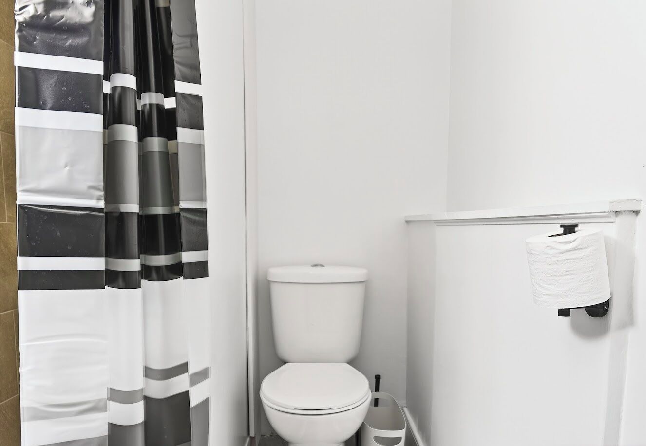 A bathroom with a toilet, a paper towel dispenser, and a striped shower curtain.