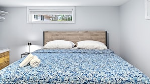 A bedroom with a bed, pillows, a lamp, and a window. - Abby’s Lodge | Modern 2BR Retreat | Prime Downtown Location (Fredericton)