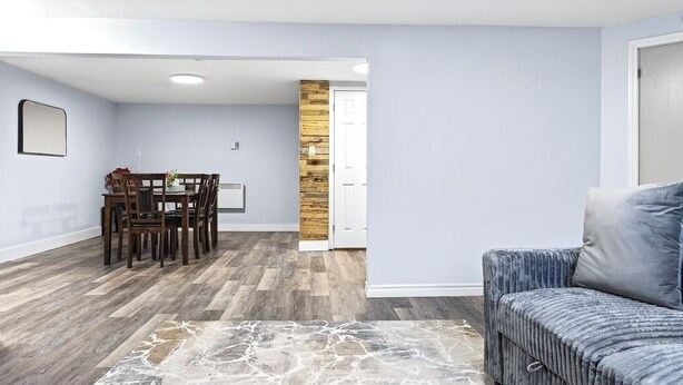 A modern living room with a dining area, a patterned rug, and a wooden accent wall. - Abby’s Lodge | Modern 2BR Retreat | Prime Downtown Location (Fredericton)