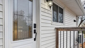 A white exterior with a glass door, a small window, and a wooden railing. - Abby’s Lodge | Modern 2BR Retreat | Prime Downtown Location (Fredericton)