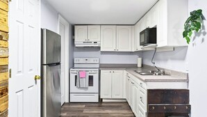 A compact kitchen with white cabinets, a stainless steel refrigerator, a microwave, and a sink. - Abby’s Lodge | Modern 2BR Retreat | Prime Downtown Location (Fredericton)